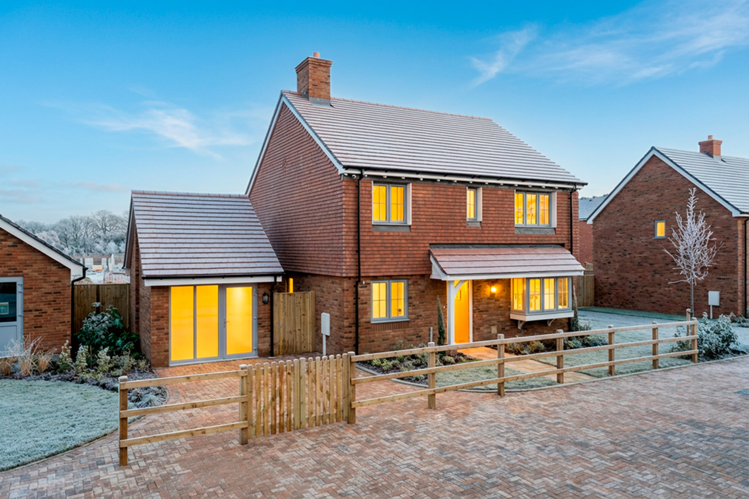2 floor red brick house on a frosty day with lights on inside and garage to the side