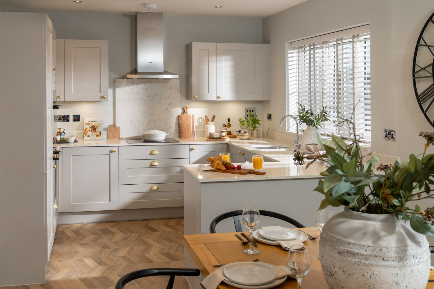 Kitchen with grey units and wooden flooring with table and chairs and vase with flowers at the forefront