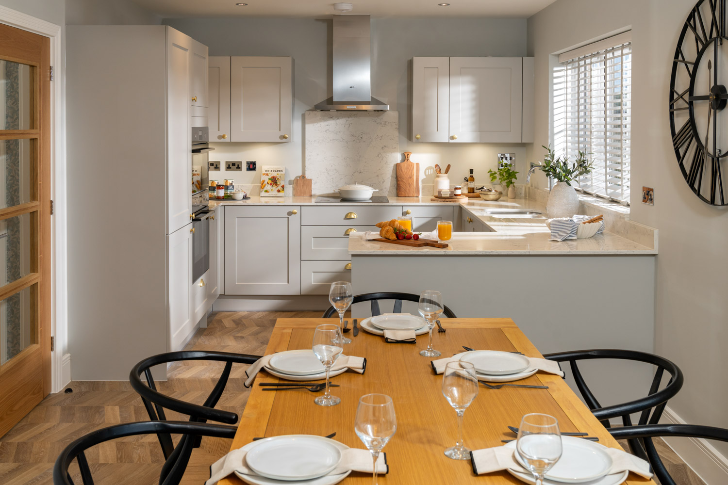 dining table and chairs a forefront of image. grey kitchen to the rear with wooden flooring and marble worktops