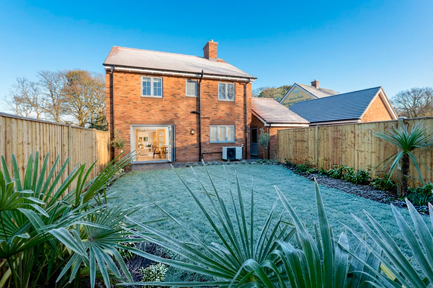 Red brick house on a frosty day with garden to the front and plants and a blue sky