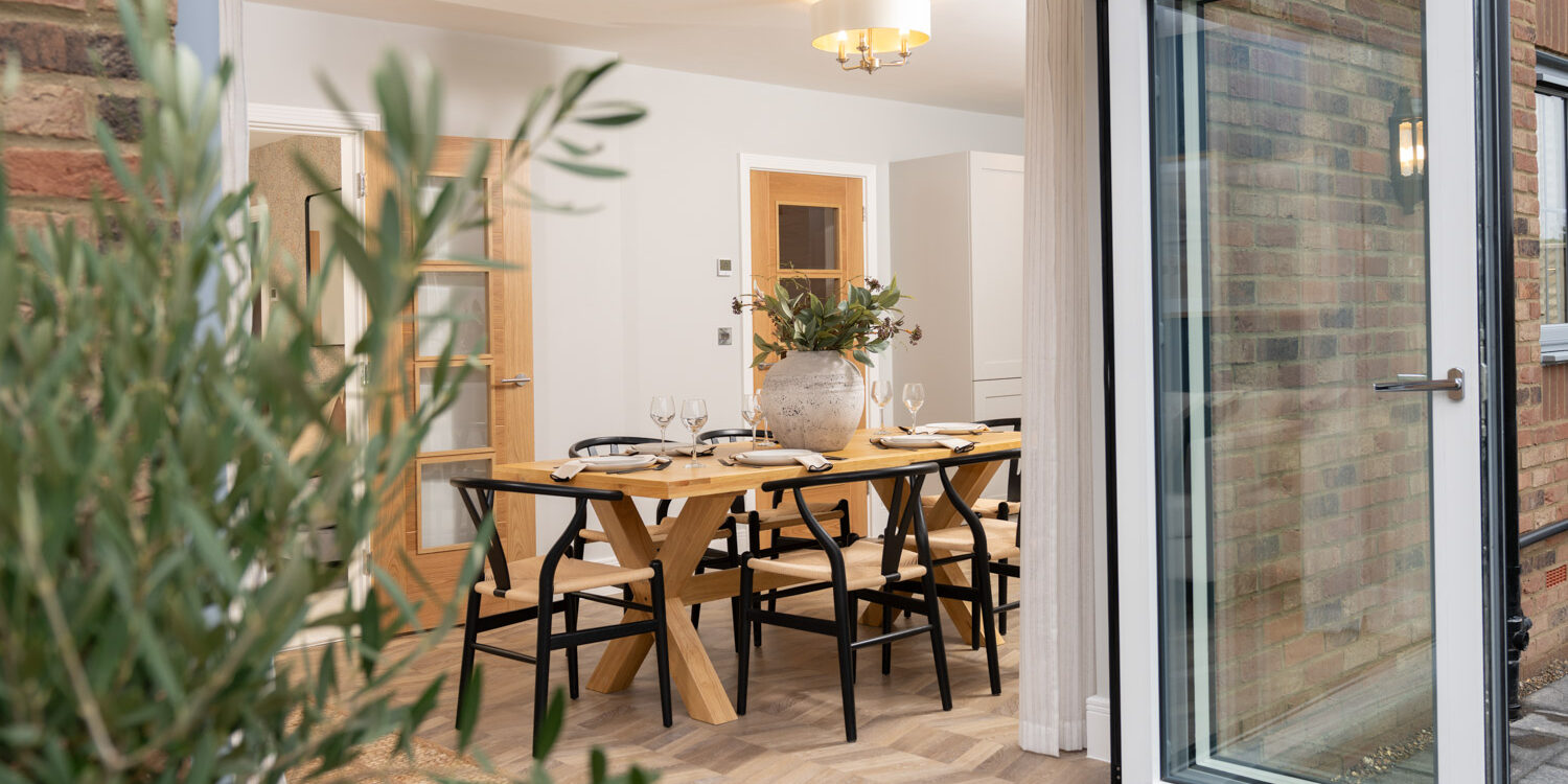 Open doors look into dining area with dining table and chairs and wooden flooring