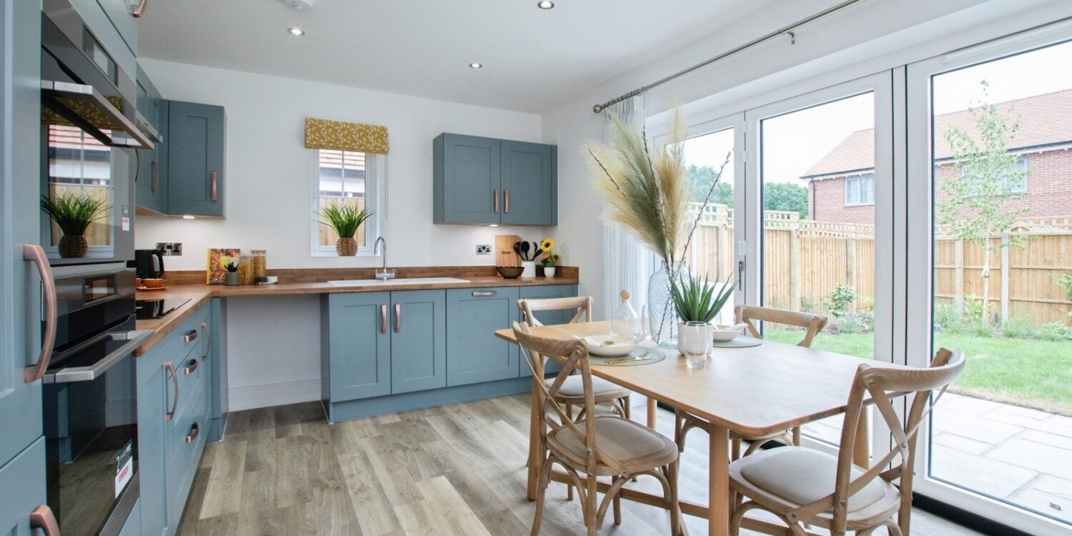 modern kitchen with bifold doors looking out to rear garden in background. blue kitchen units and wooden flooring