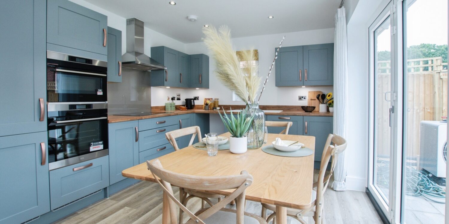 Modern fitted kitchen with blue kitchen units in the background and light wooden dining table to the front